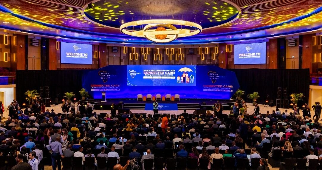 Wide view of the Africa HealthTech Summit plenary hall, with a large stage, welcome screens and a full audience.