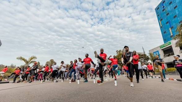 A wide view of many participants doing a mass exercise session on a Kigali street under a cloudy sky.